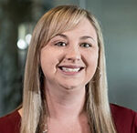 Professional headshot of Autumn Roberts, Implementation Program Coordinator at Sydney Administrators. She has long straight blonde hair with bangs and is smiling warmly at the camera. She is wearing a burgundy/deep red top with a necklace against a slightly blurred office background.